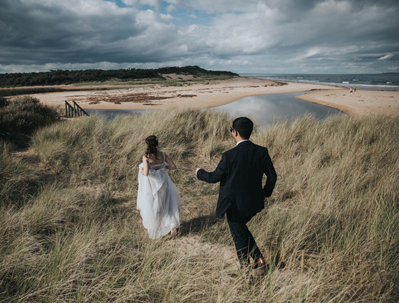 Bride and groom run down the sand banks together